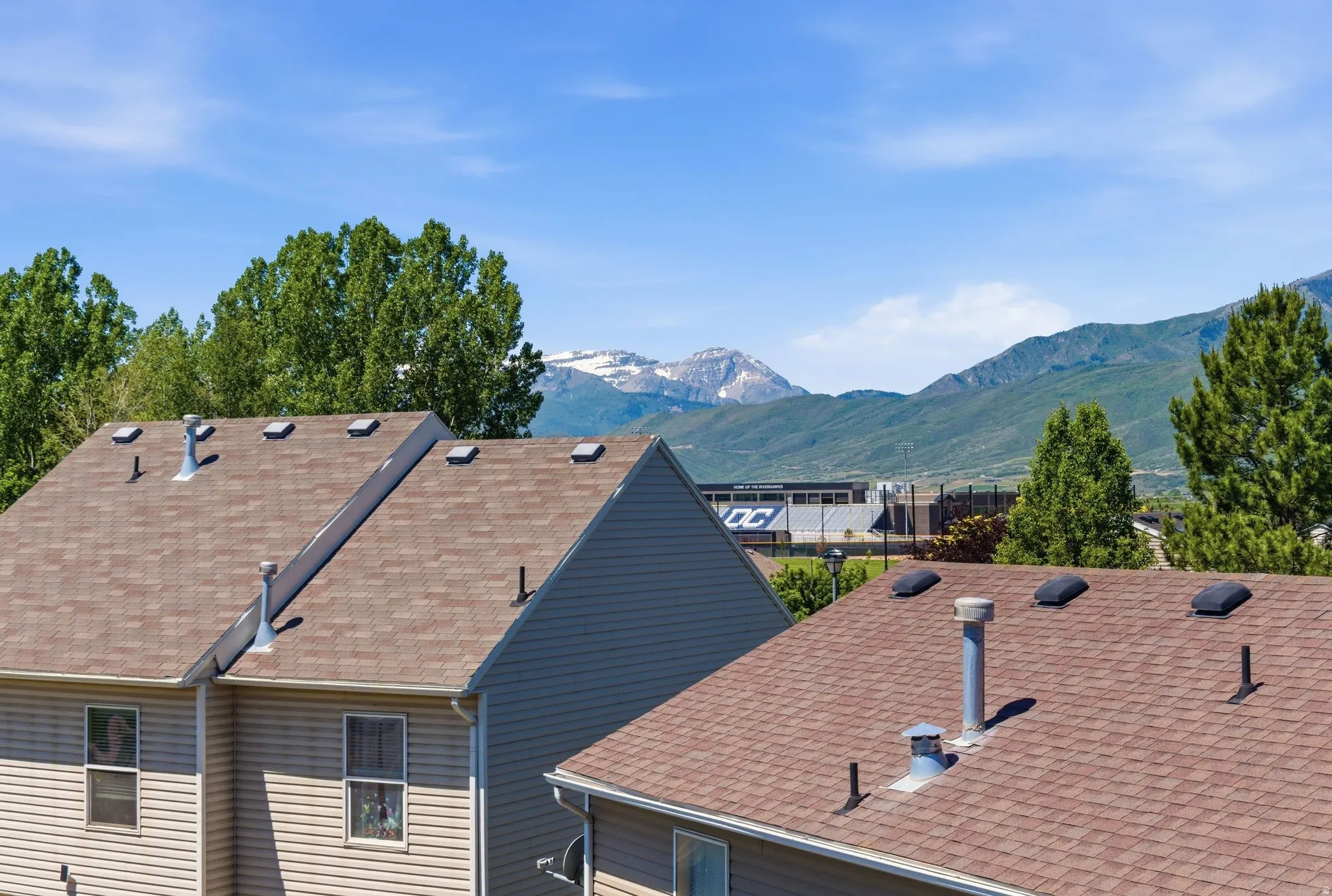Mountain backdrop with a clear sky, mature trees, and shingle roofing