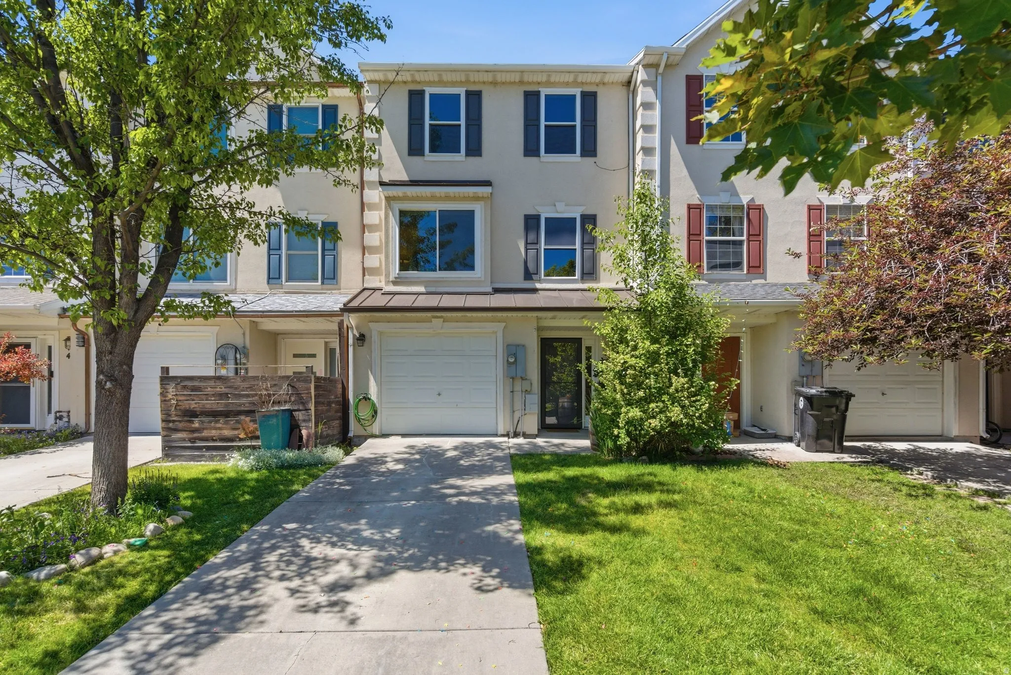 Multi-level townhome featuring a neutral stucco exterior, bay windows with contrasting shutters, and an integrated single-car garage