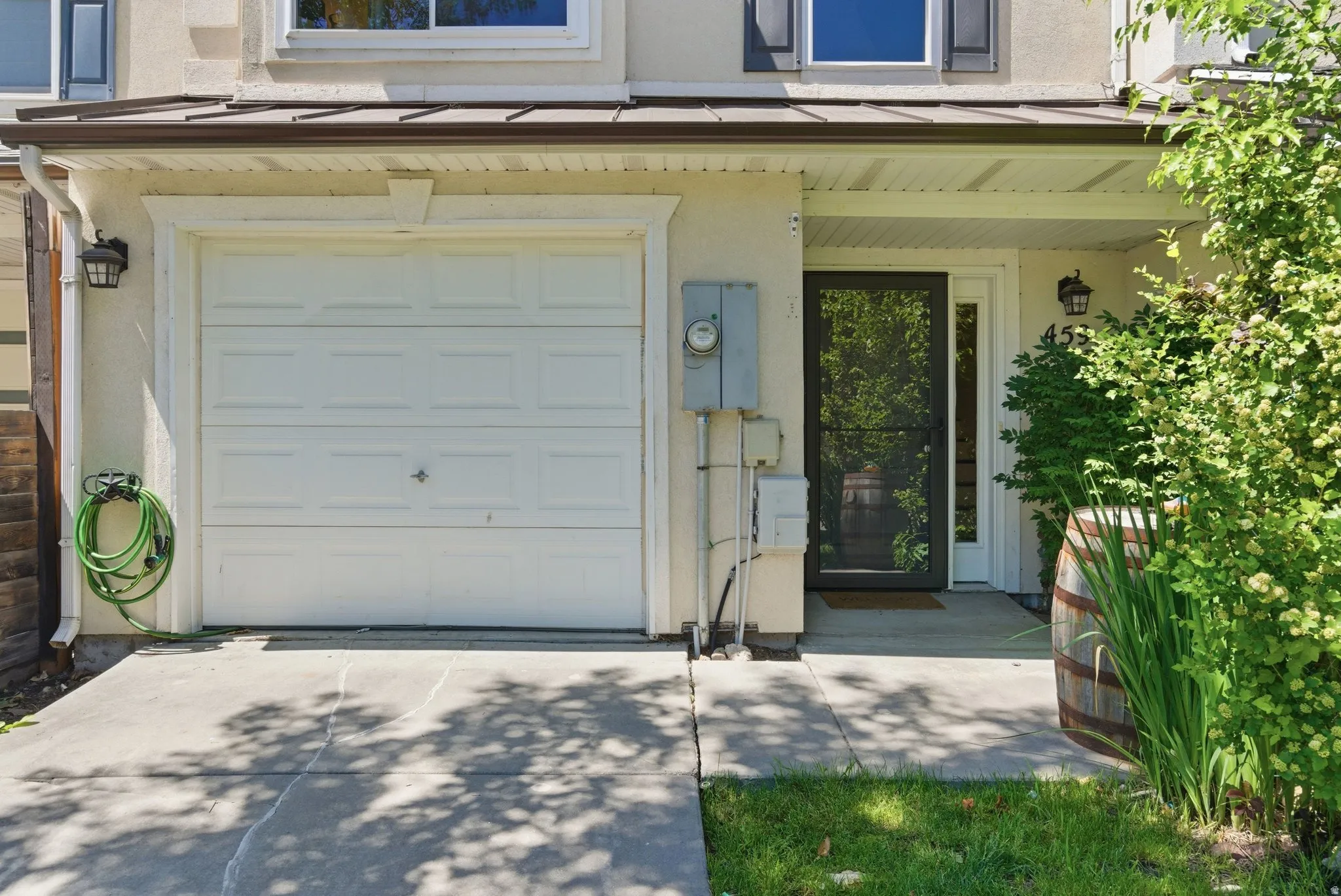 Exterior featuring a panel garage door, concrete driveway, covered porch entrance, and mature landscaping