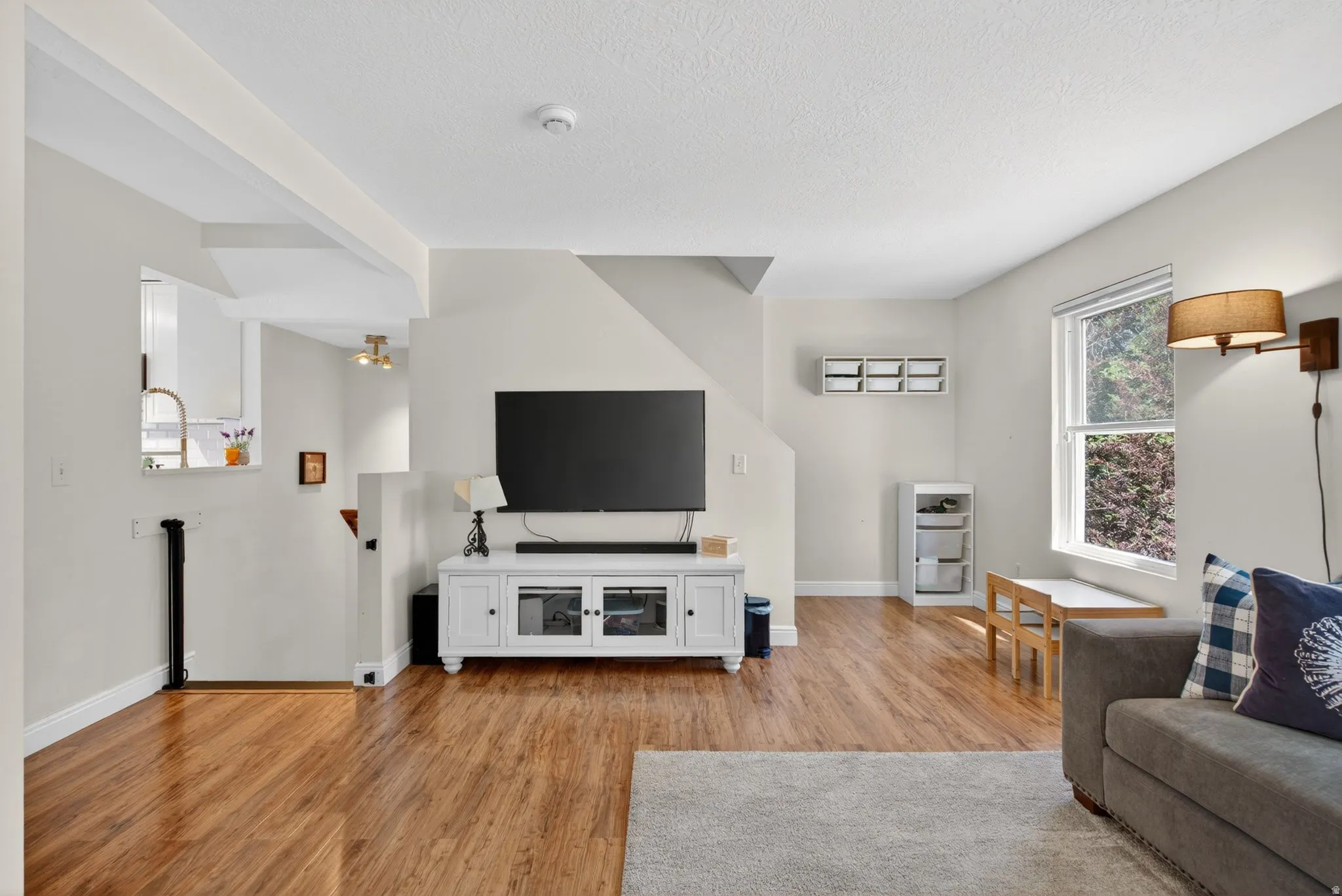 Spacious living area featuring wood-finish flooring, a neutral color palette, and ample natural light from a prominent window