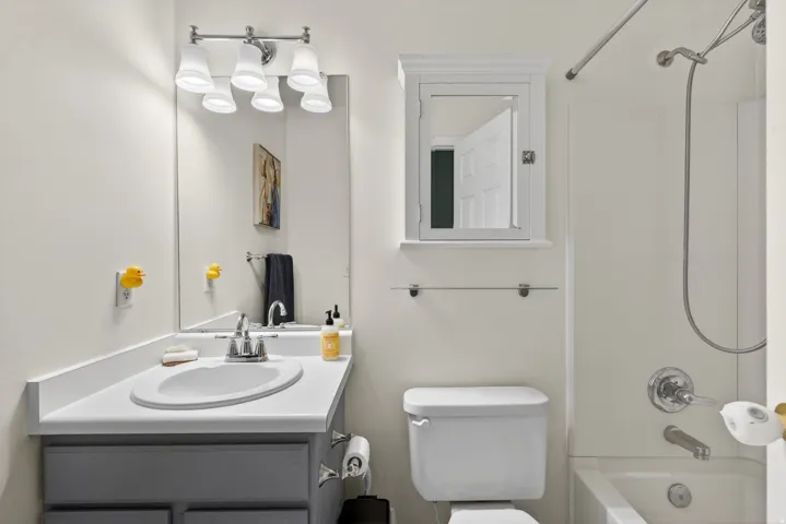 Bathroom featuring a vanity with an integrated sink, a medicine cabinet, a full mirror, and a shower-over-tub combination with a curved shower rod
