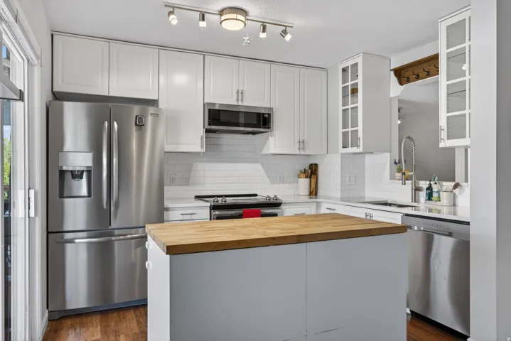 Contemporary kitchen featuring white cabinetry, stainless steel appliances, butcher block island, white subway tile backsplash, and wood-finish flooring