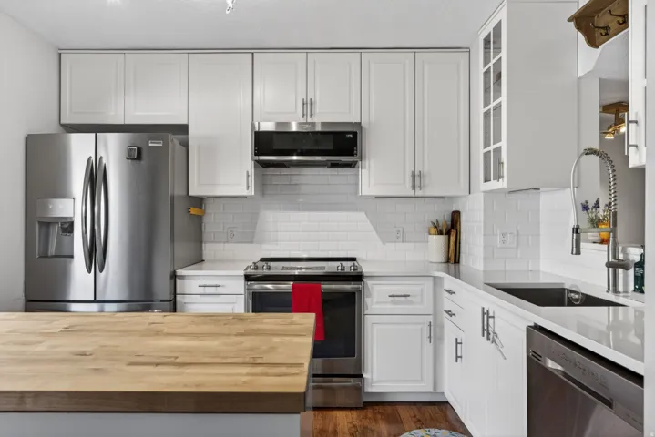 Kitchen featuring white shaker-style cabinetry, stainless steel appliances, white subway tile backsplash, light-toned countertops, and a wood-finish island countertop