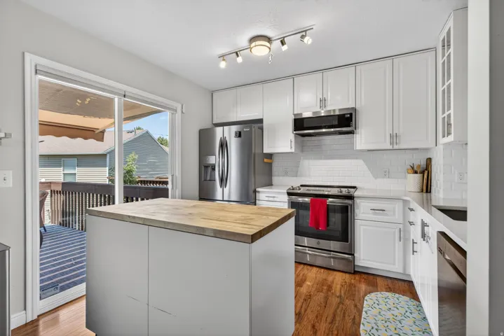 Contemporary kitchen featuring a center island with a wood-finish countertop, white cabinetry, stainless steel appliances, a subway tile backsplash, and wood-finish flooring