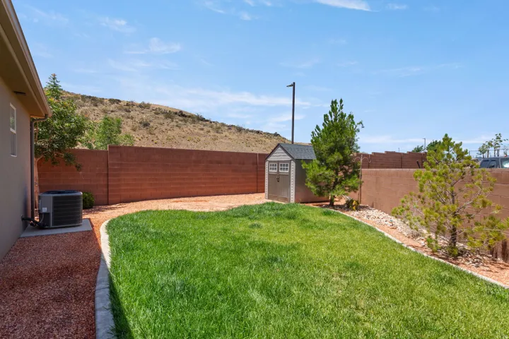 Expansive rear yard featuring green lawn, red rock landscaping, and mature plantings