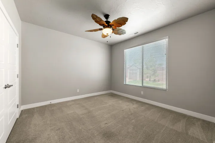 Carpeted room featuring a large window with horizontal blinds, a decorative ceiling fan, and a white paneled door