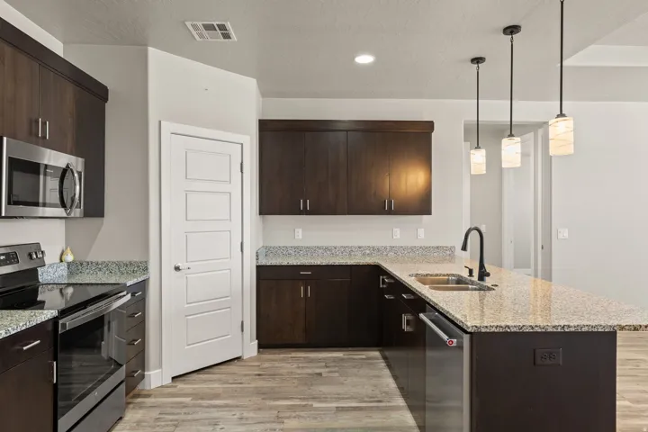 Kitchen featuring dark wood-finish cabinetry, speckled countertops, stainless steel appliances, and a kitchen island with sink and pendant lighting