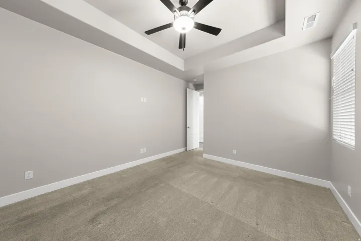 Spacious room featuring tray ceilings, neutral carpeting, and a ceiling fan with integrated lighting
