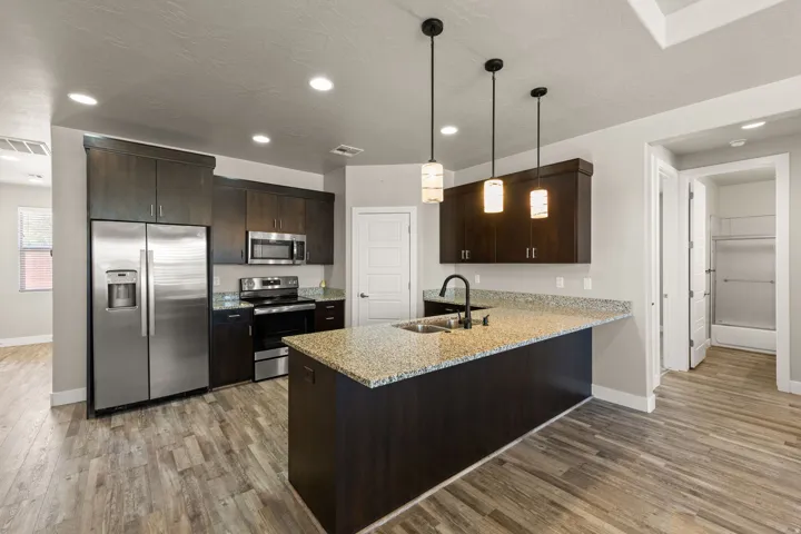 Modern kitchen featuring an expansive island with a granite-style countertop, dark wood-finish cabinetry, stainless steel appliances, and pendant lighting
