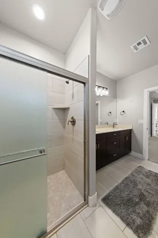 Walk-in shower with tiled walls and floor, complete with a built-in shelf and brushed nickel fixtures