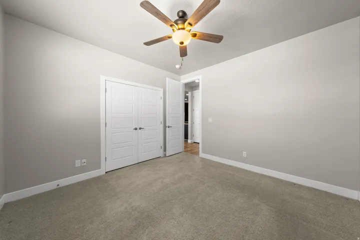 Neutral-toned room featuring a ceiling fan with integrated lighting, textured carpeting, and double panel doors