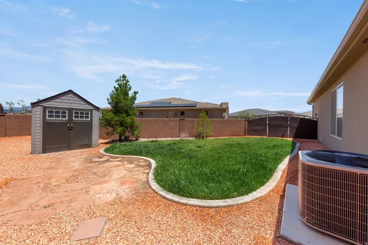 Expansive backyard featuring a central lawn area, gravel landscaping, a detached storage shed, a mature evergreen tree, and a concrete perimeter wall