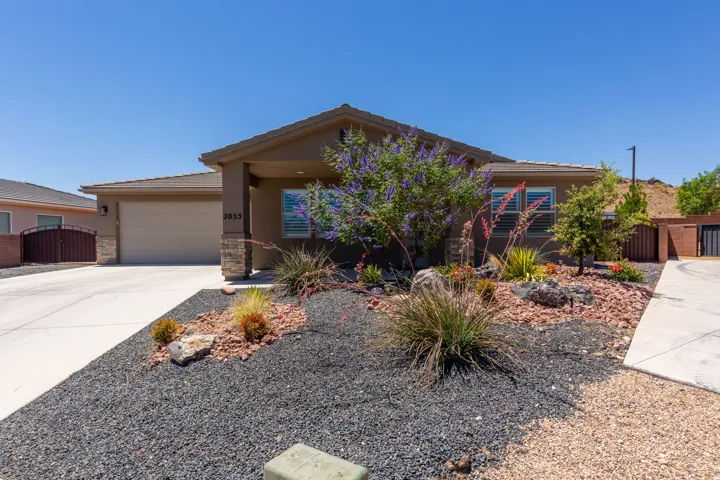 Contemporary stucco exterior with stone accents, featuring a two-car garage, a concrete driveway, and a low-maintenance xeriscape front yard