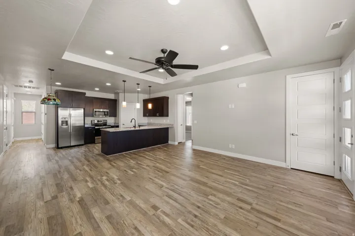 Open-concept living space featuring wood-finish flooring, a contemporary kitchen with stainless steel appliances, dark cabinetry, and pendant lighting