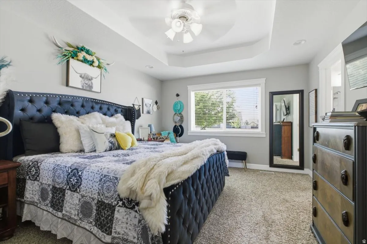 Recessed tray ceiling with a ceiling fan, light gray wall paint, and plush carpet flooring