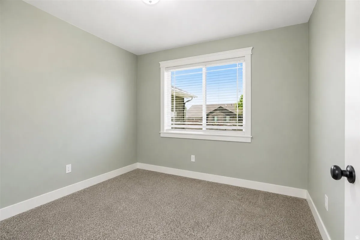 Neutral-toned room featuring a window with white trim, gray carpet, and light green walls