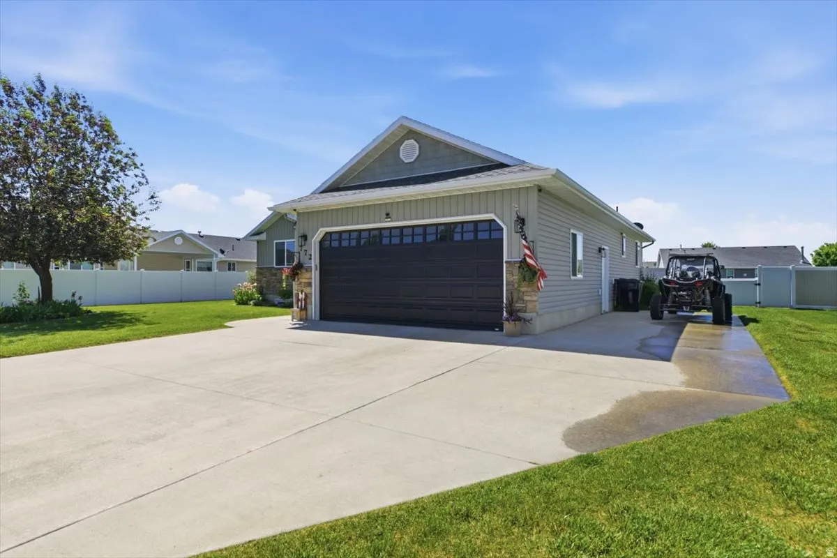 Side-load garage with a dark panel door, light grey siding, and stone accents