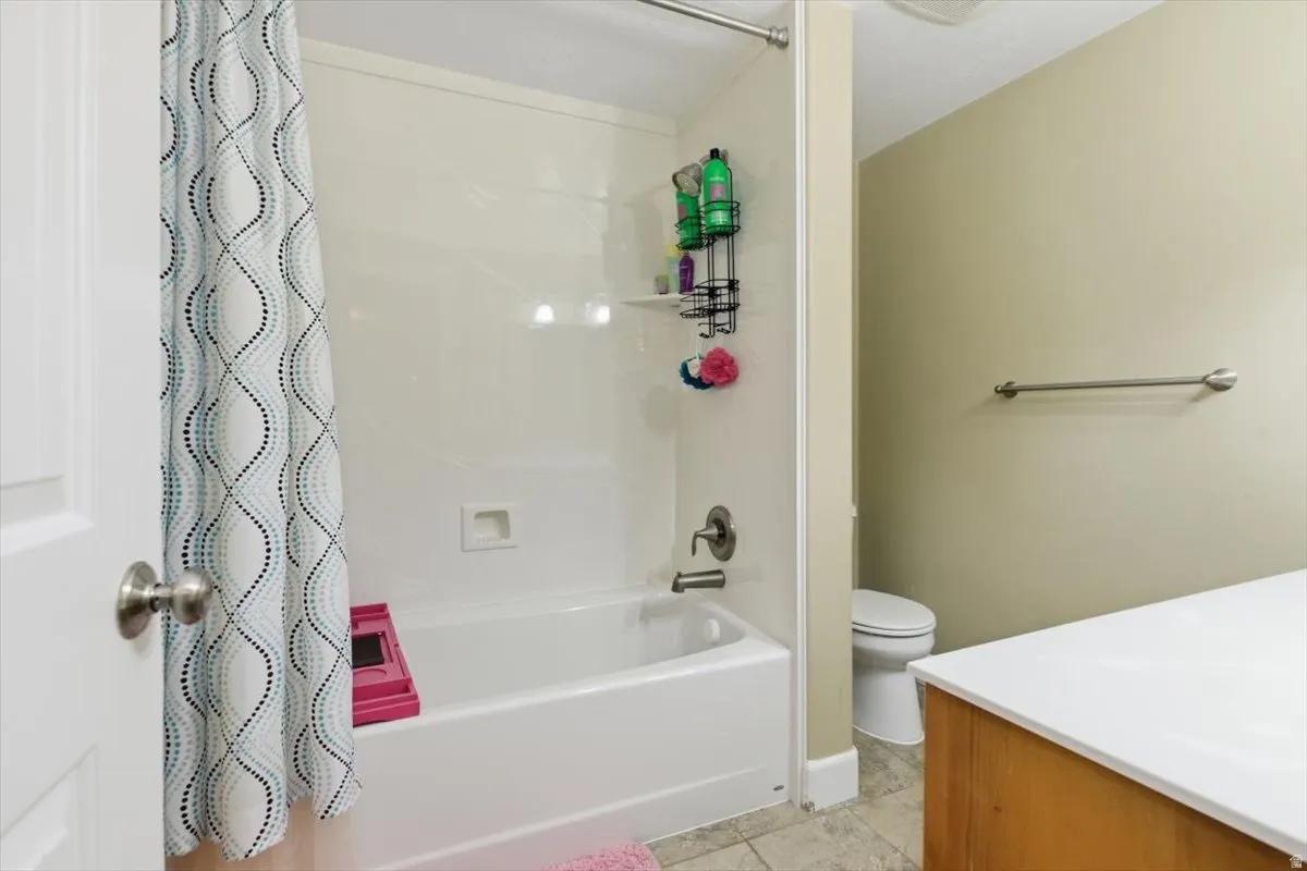 Bathroom featuring a white tub and shower combination with brushed nickel fixtures, a neutral wall color, and a wood-finish vanity with a white countertop