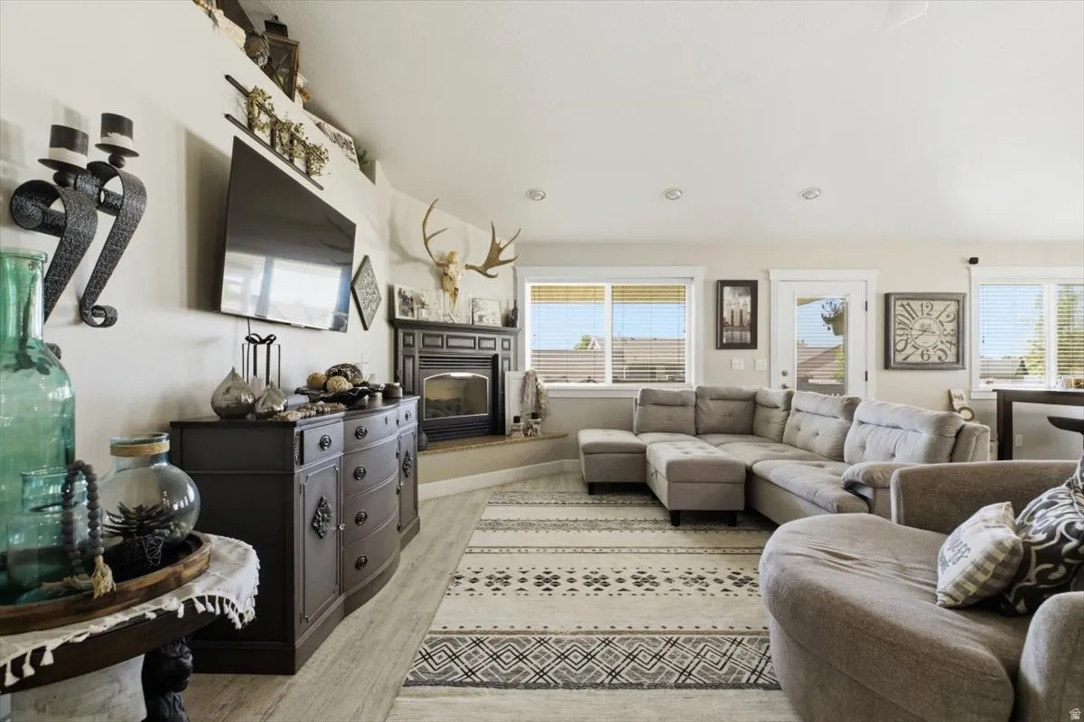 Spacious living area featuring light wood-finish flooring, recessed lighting, and multiple windows with blinds