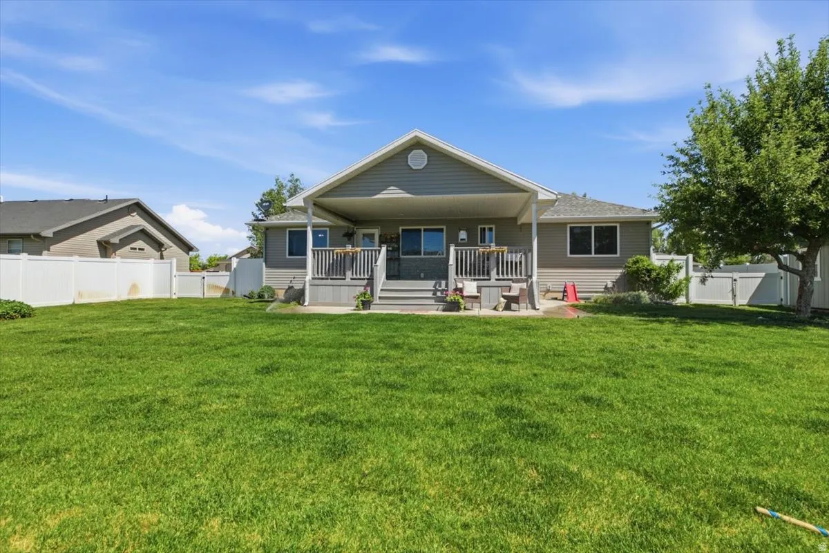 Expansive backyard with a large, manicured lawn, a covered porch, an open deck, and white privacy fencing