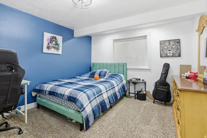 Carpeted bedroom featuring a window with blinds, a ceiling-mounted light fixture, and a built-in architectural beam