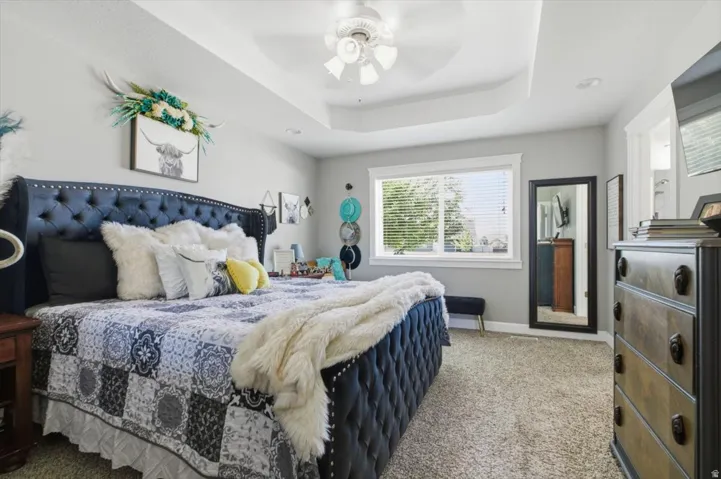 Recessed tray ceiling with a ceiling fan, light gray wall paint, and plush carpet flooring