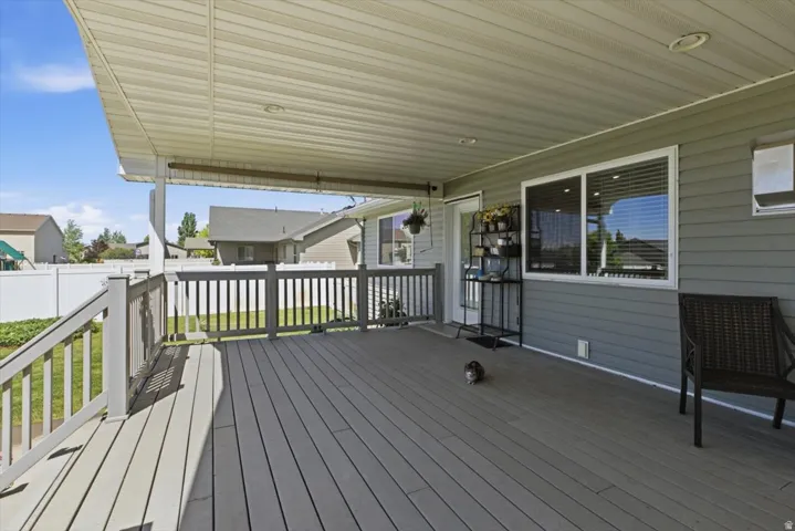 Expansive covered deck featuring a textured composite surface, white railing, recessed lighting, and direct access to interior via a glass-paneled door