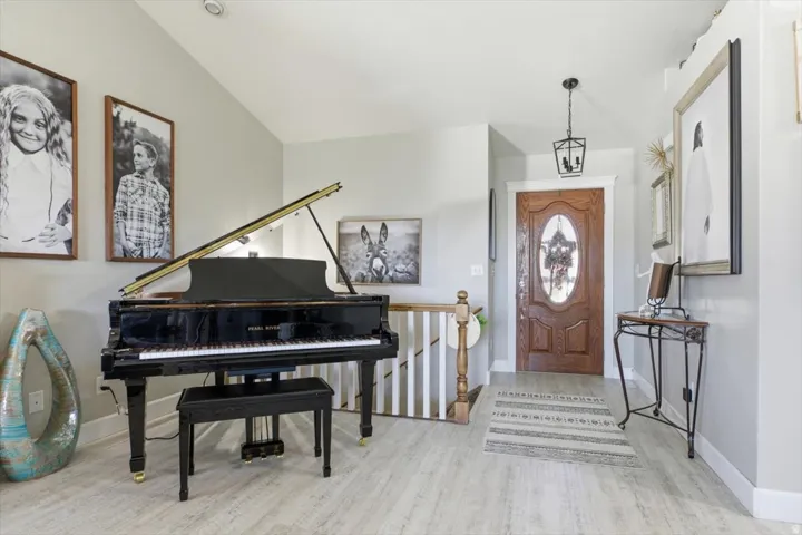Foyer featuring wood-finish flooring, a wood entry door with an oval glass insert, a black lantern-style pendant light, and a white staircase with a wood railing