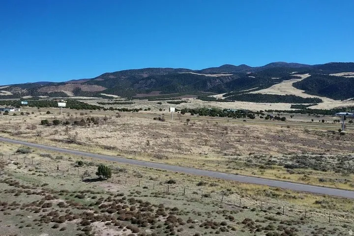 Expansive undeveloped land featuring a paved road, scattered natural vegetation, and distant mountain ranges