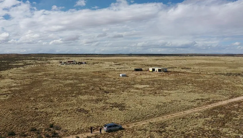Expansive rural landscape featuring a single-story structure, multiple smaller outbuildings, and a visible dirt road