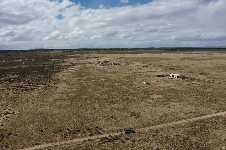 Expansive open land featuring a single-story structure, multiple outbuildings, and a visible track road
