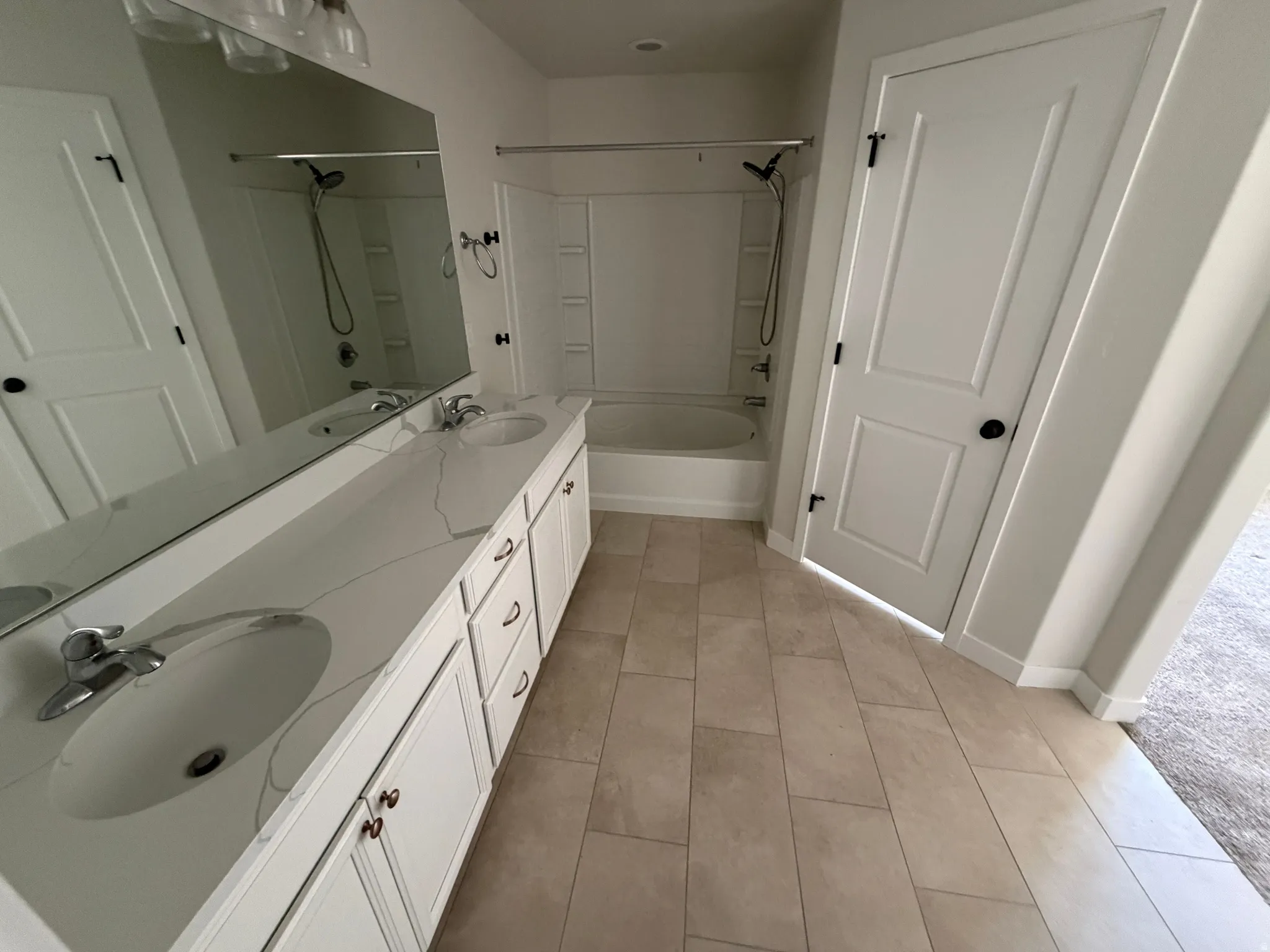 Bathroom featuring a dual-sink vanity with a light-toned countertop, a full-width mirror, and an integrated bathtub with a shower