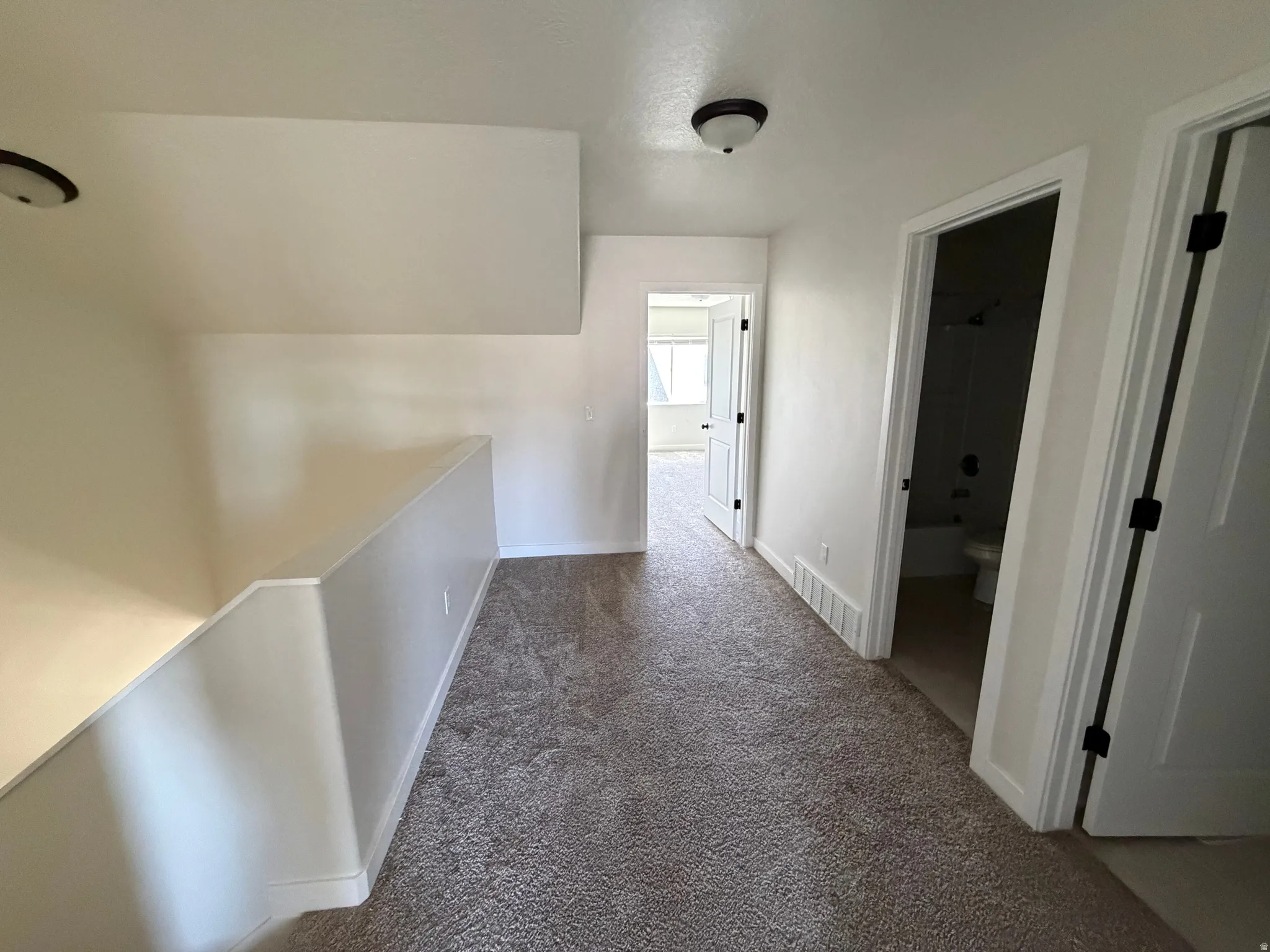 Hallway featuring textured carpeting, white baseboards, and white interior doors with black hardware