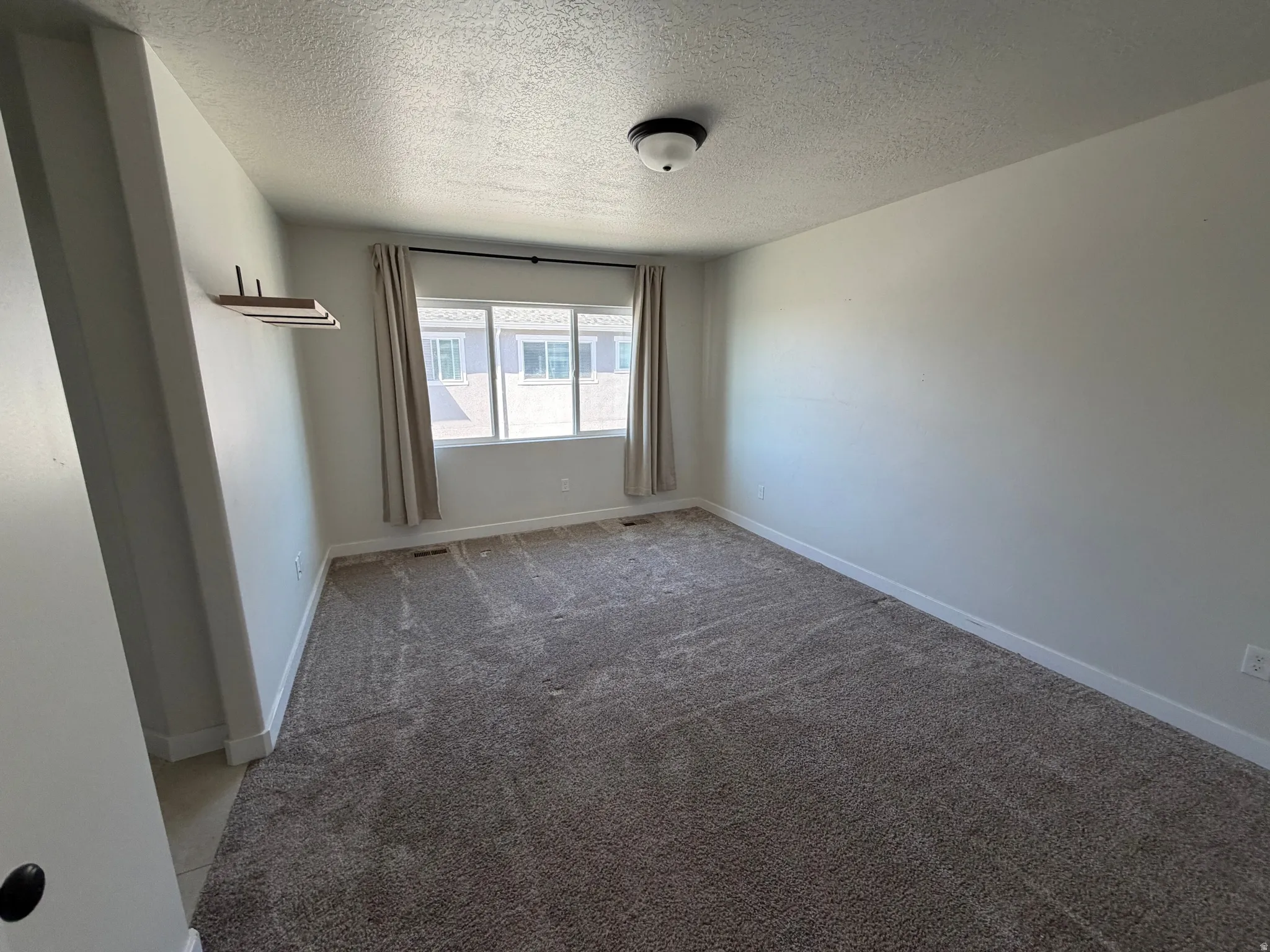 Carpeted room featuring a large window, neutral wall paint, and a built-in floating shelf