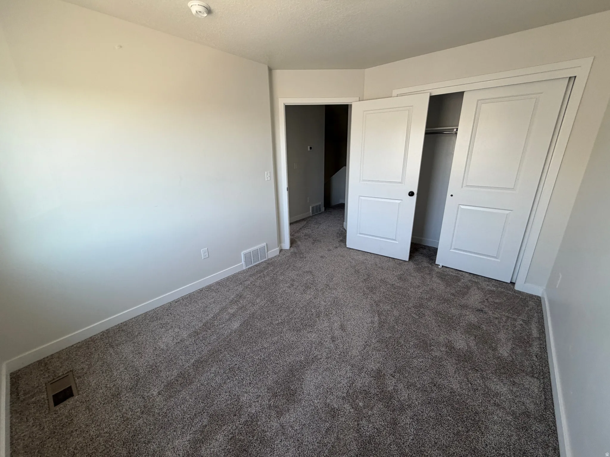 Bright interior room featuring neutral wall paint, gray carpeting, white baseboards, and a bi-fold closet with white panel doors