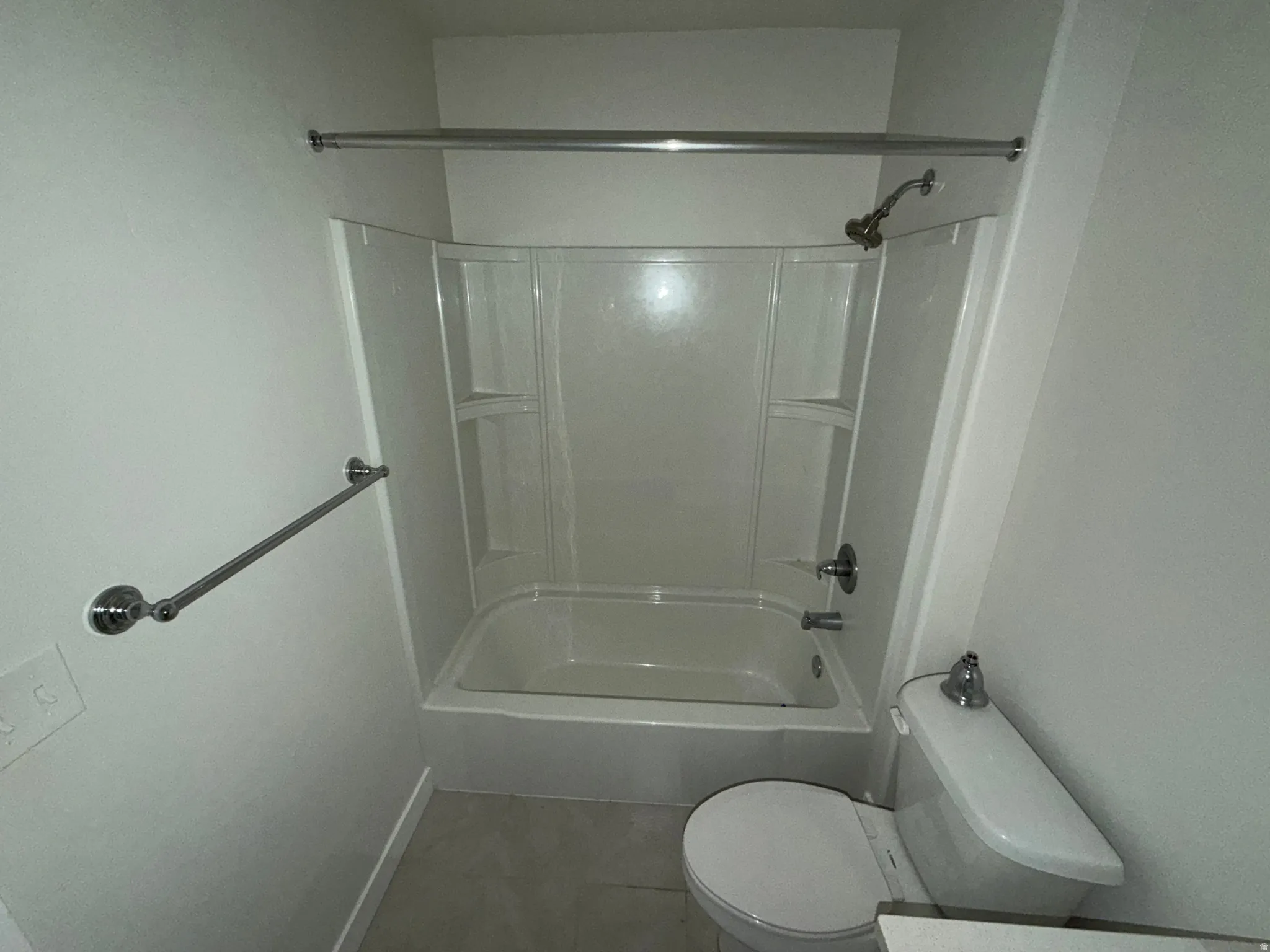 Tub and shower combination with a curved shower curtain rod, chrome fixtures, and a white toilet