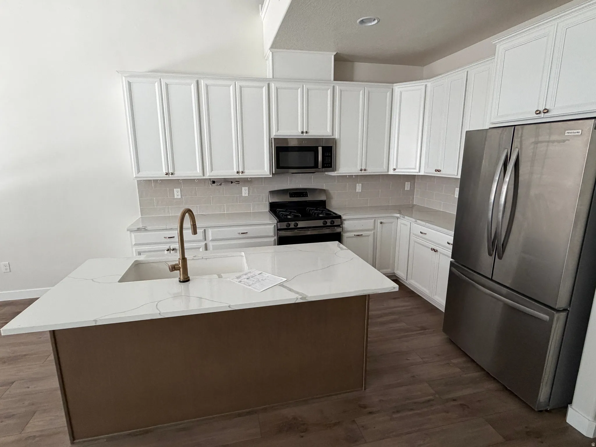 Modern kitchen featuring a central island with an undermount sink, white cabinetry, stainless steel appliances, a subway tile backsplash, and wood-finish flooring