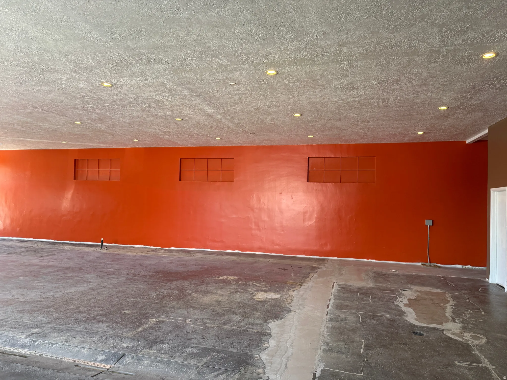 Spacious interior with an orange accent wall, recessed lighting, and exposed concrete flooring