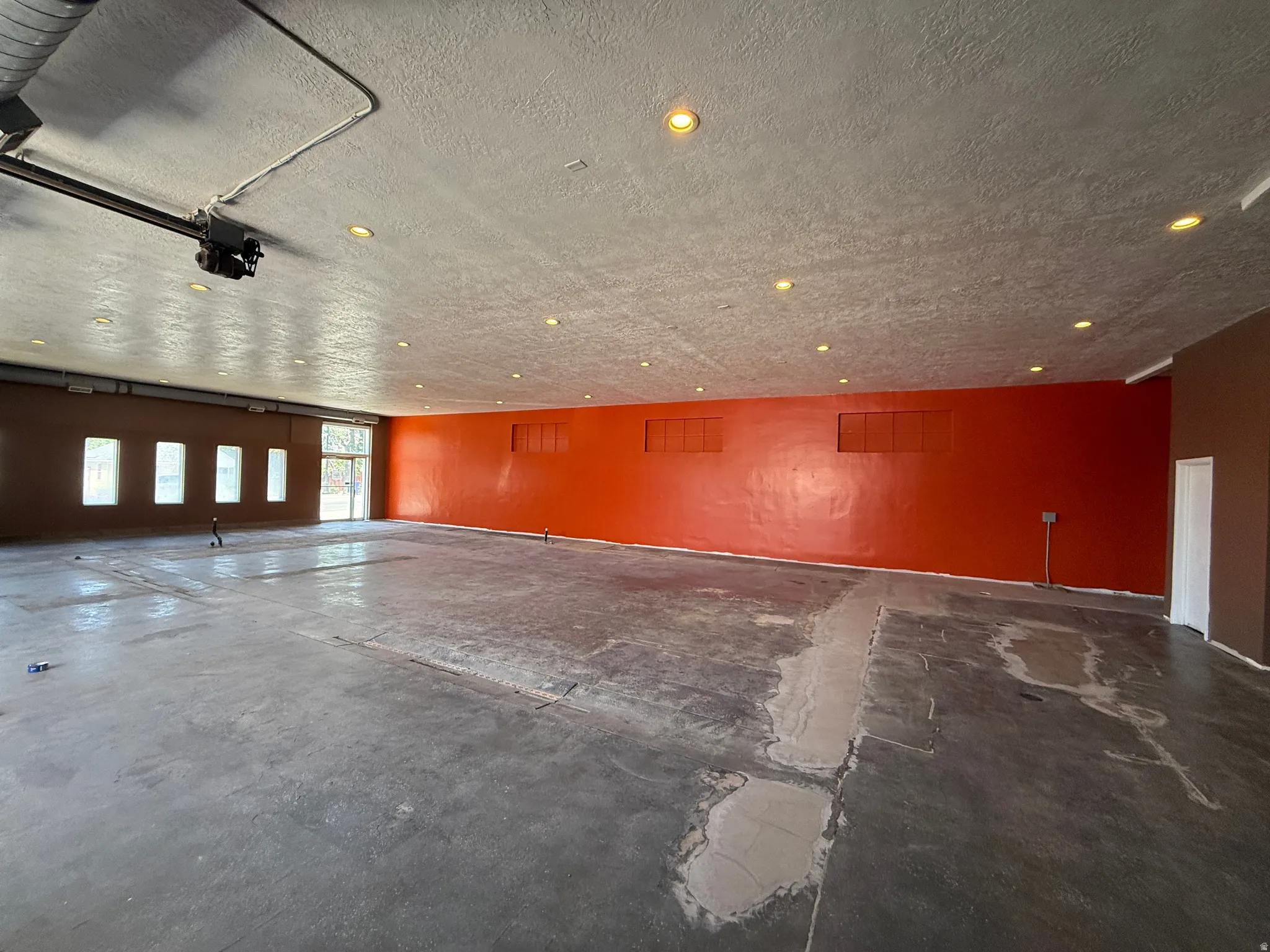 Expansive interior space featuring a concrete floor, recessed ceiling lighting, exposed conduit, and multiple windows