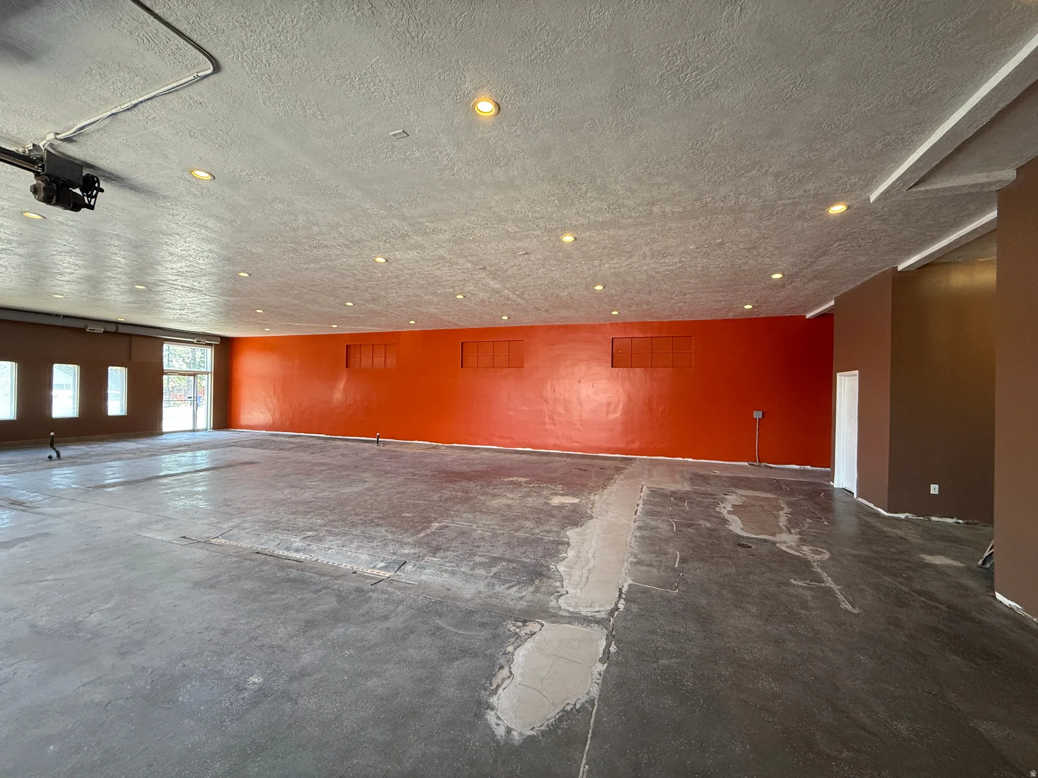 Spacious commercial interior featuring a concrete floor, recessed lighting, and a prominent orange accent wall