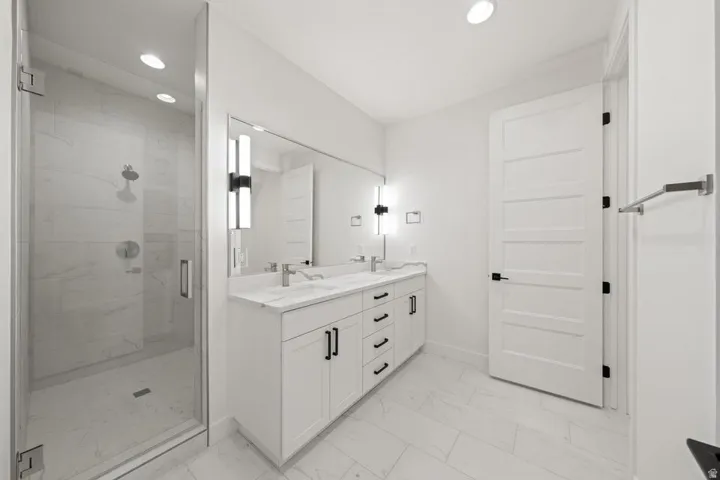 Modern bathroom featuring a frameless glass shower enclosure, a dual vanity with a white countertop, and contemporary wall-mounted light fixtures