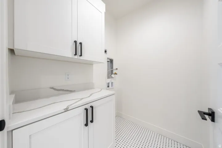 White shaker-style cabinetry with matte black hardware, a light-toned countertop with distinct veining, and a black and white mosaic tile floor