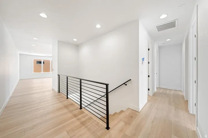 Contemporary interior featuring light wood-finish flooring throughout, a modern black horizontal bar railing, white walls, recessed ceiling lighting, and crisp white trim
