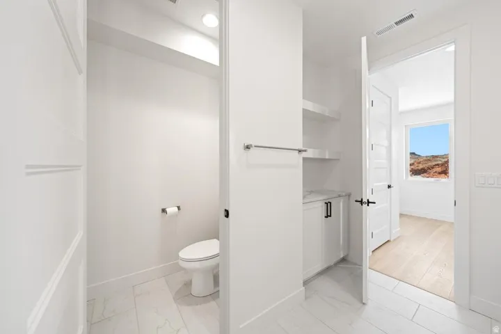 Modern powder room featuring white paneled walls, recessed lighting, and large format marble-look tile flooring