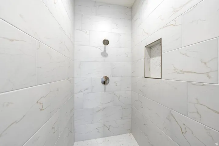 Shower enclosure featuring white marble-look tile, a built-in niche with herringbone tile backing, and chrome fixtures