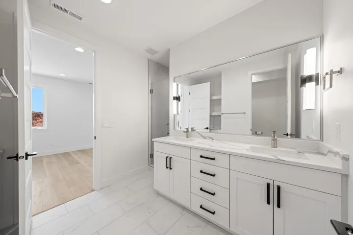 Bathroom with dual vanity featuring white shaker-style cabinetry and a light-colored countertop