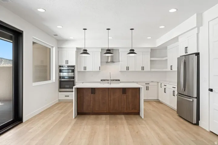 Modern kitchen featuring white cabinetry, stainless steel appliances, a center island with wood-finish cabinetry, light wood-finish flooring, and recessed lighting