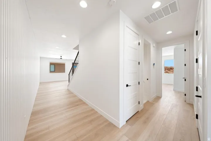 Bright interior hallway featuring wood-finish flooring, recessed lighting, and contemporary paneled doors with matte black hardware