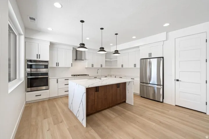 Modern kitchen featuring a waterfall island with a wood-finish base, white cabinetry, stainless steel appliances, and light wood-finish flooring
