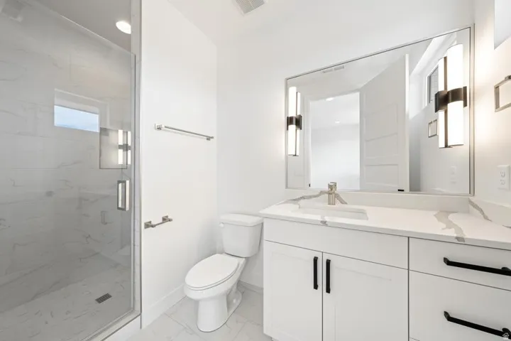 Contemporary bathroom featuring a spacious glass-enclosed shower, white vanity with stone-look countertop, and modern lighting fixtures